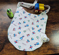 Adult sized bib - white with vehicle pattern, lying flat on wooden surface surrounded by toys