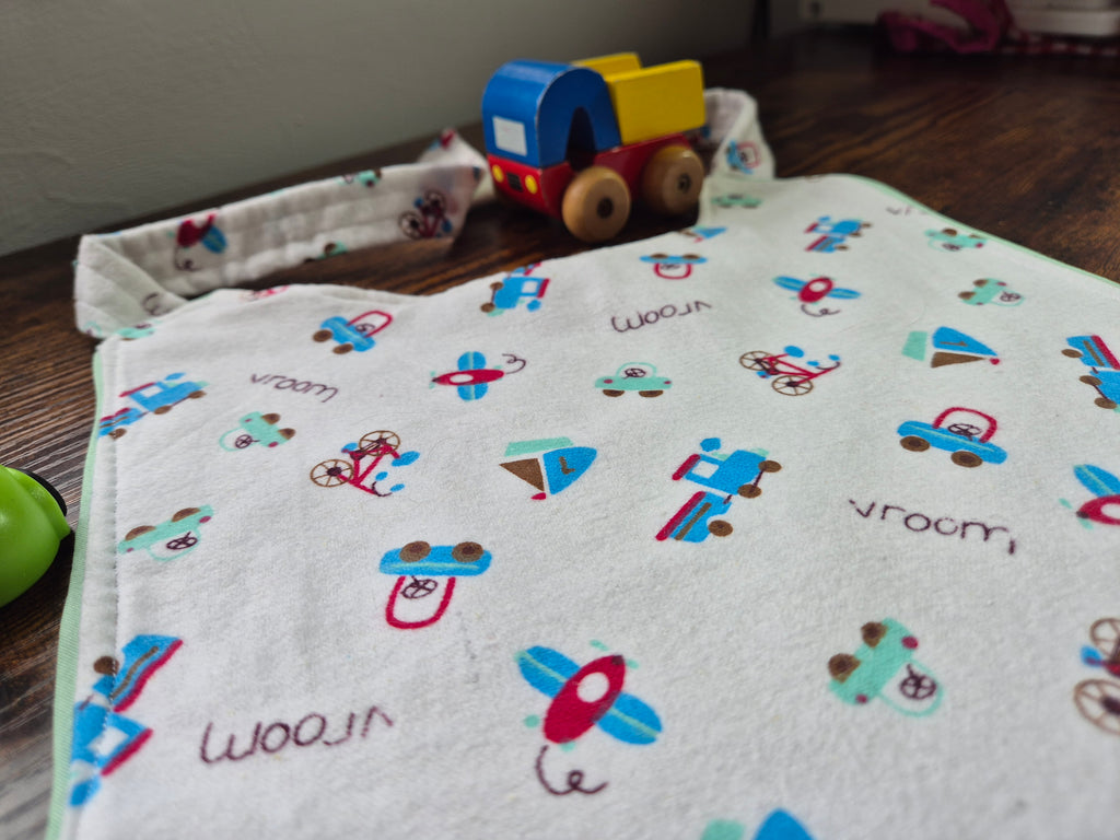 Close up of adult baby bib with vehicle and airplane patterns on a wooden surface with a toy car.