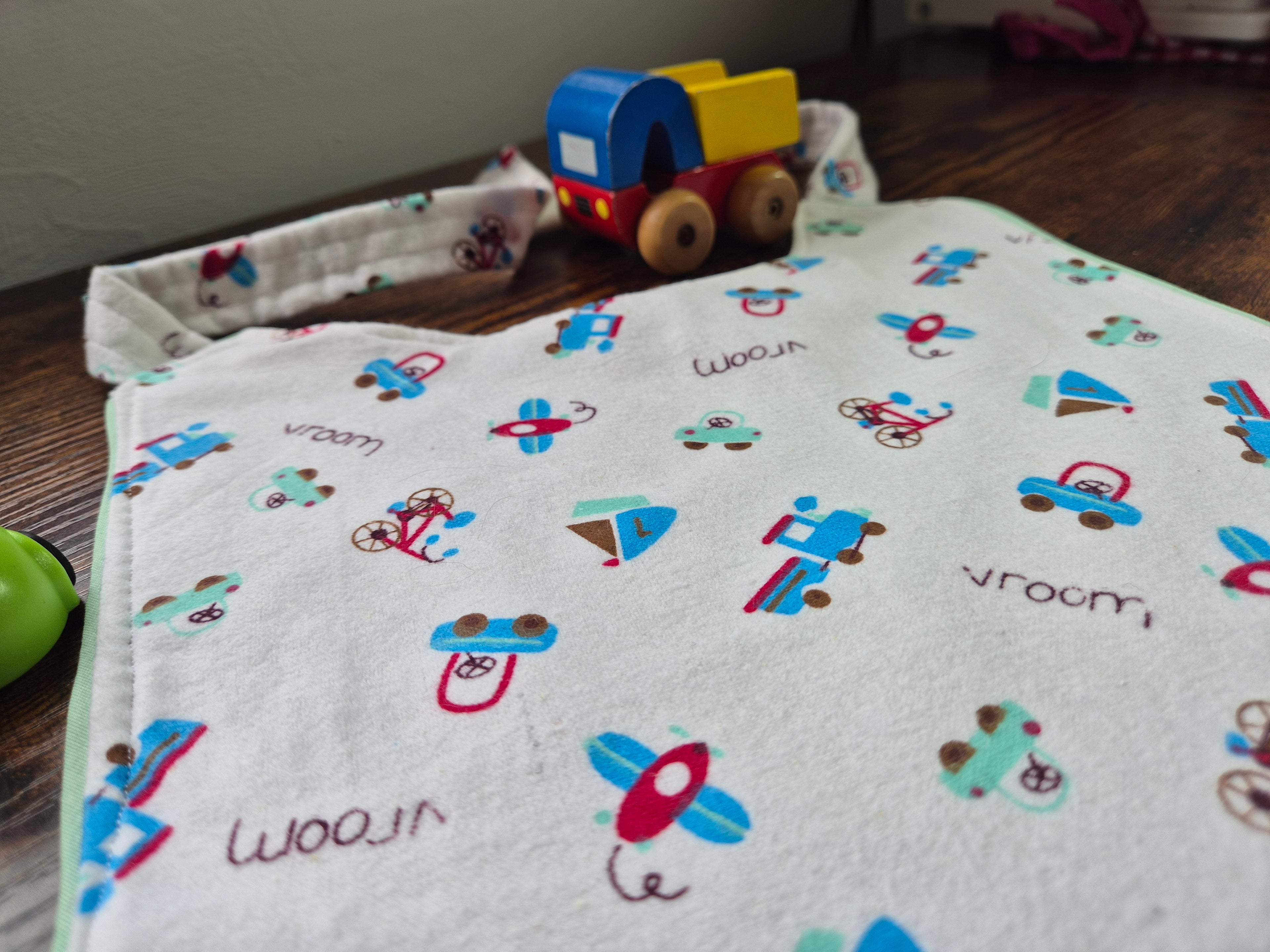 Close up of adult baby bib with vehicle and airplane patterns on a wooden surface with a toy car.