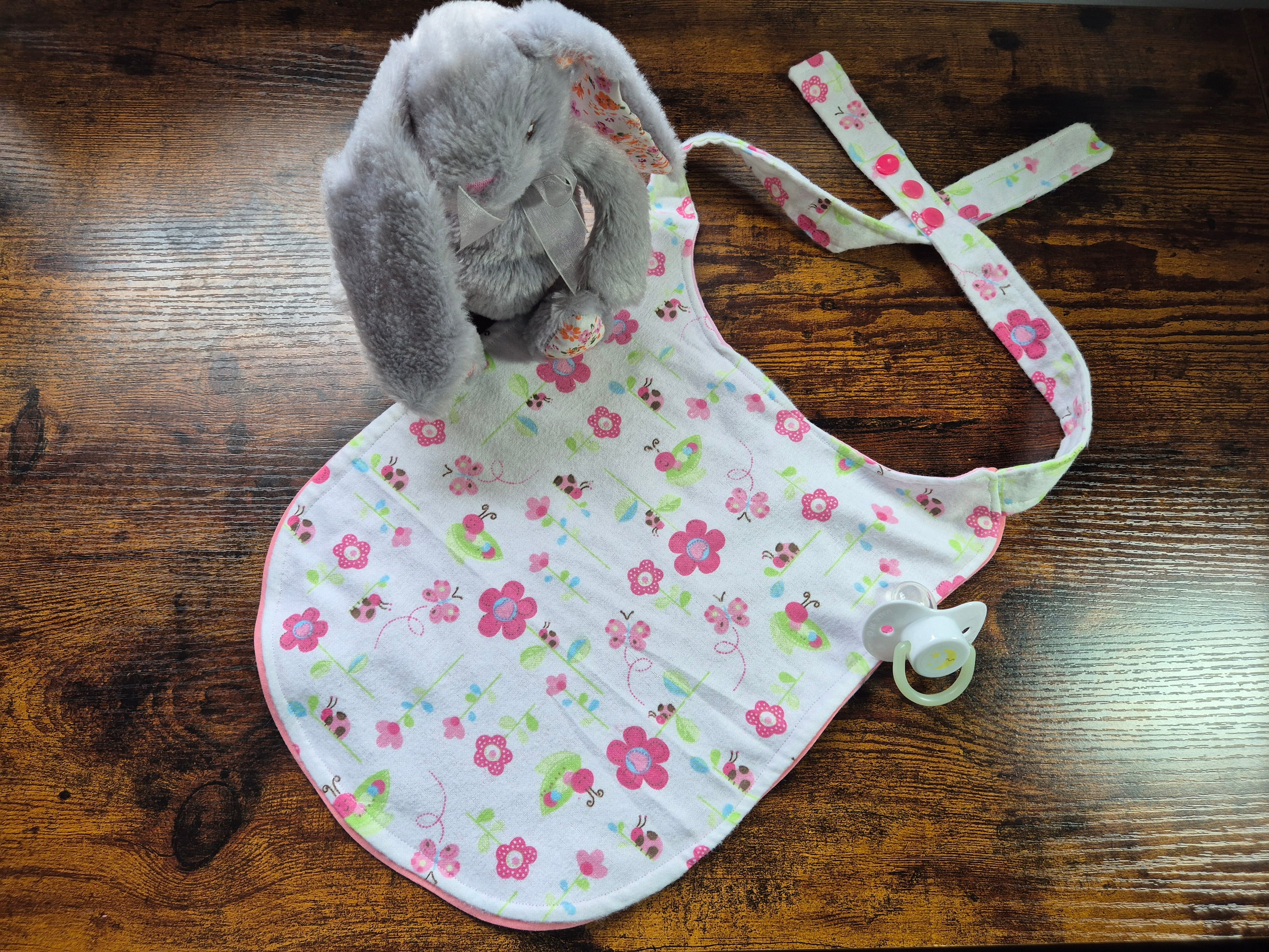 Iron in the Kinks Nom Nom ABDL bib in white with pink flowers and ladybird print, back view showing pink bound edges and snap fastener