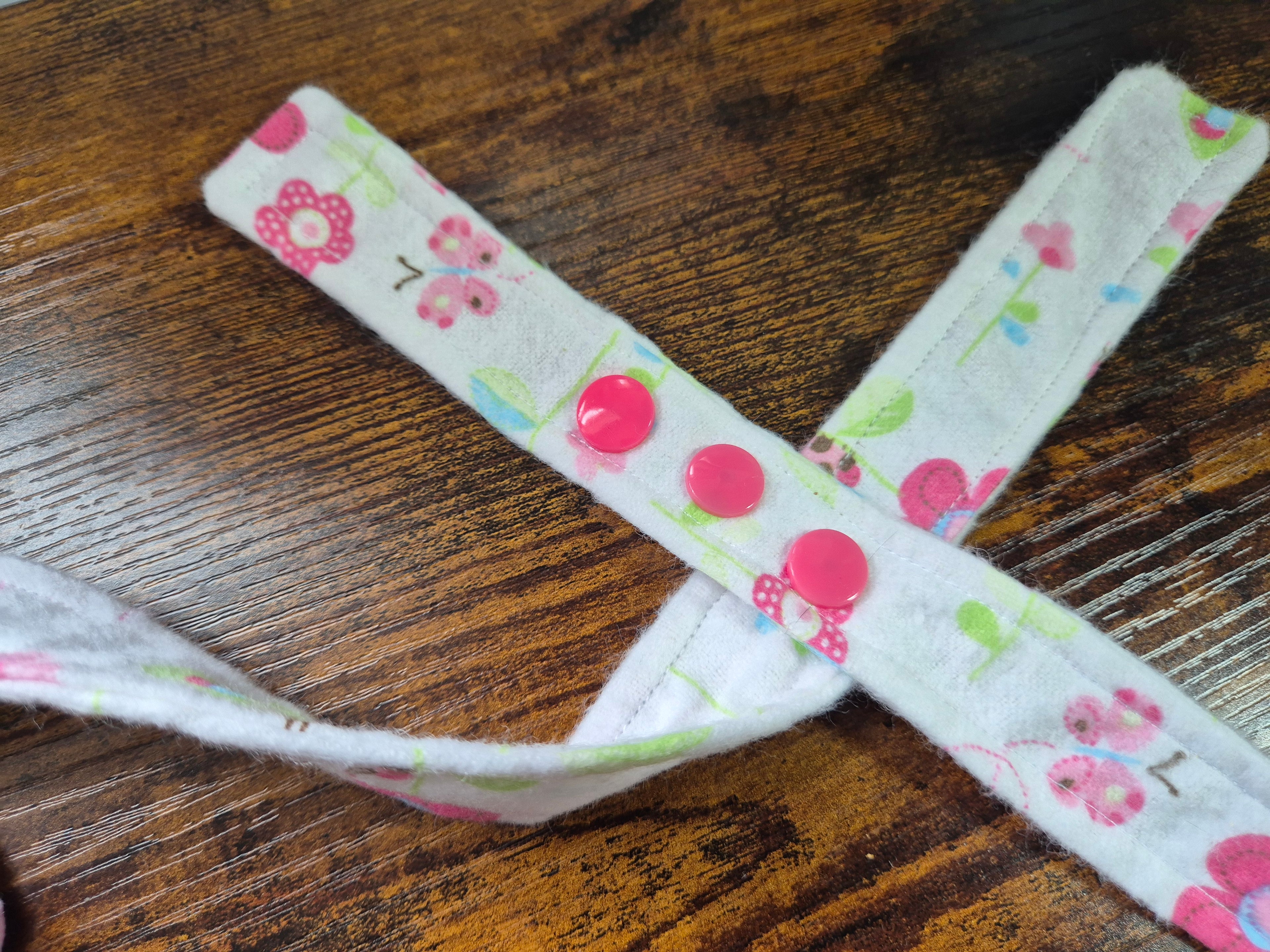Fabric strap with floral pattern showing coloured snap fasteners on a wooden surface