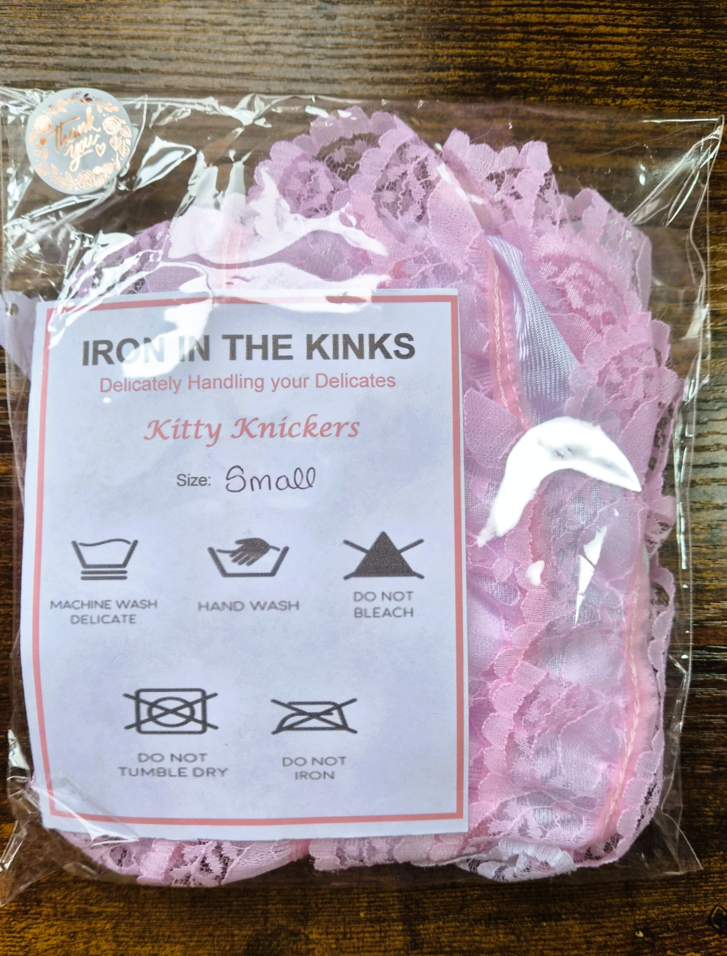 Iron in the Kinks Kitty Knickers in pink lace in clear packaging with care label, size Small — machine wash delicate, hand wash, do not bleach, tumble dry, or iron