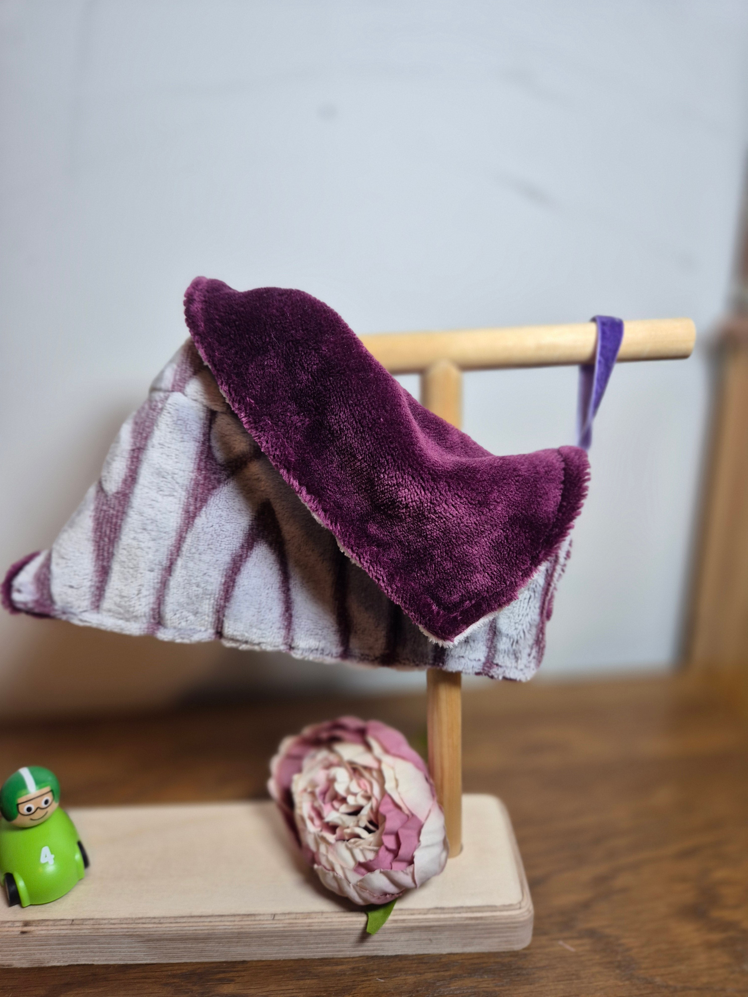 Close up of comforter draped over stand, ribbon loop attached to wood, flower and toy on stand. 