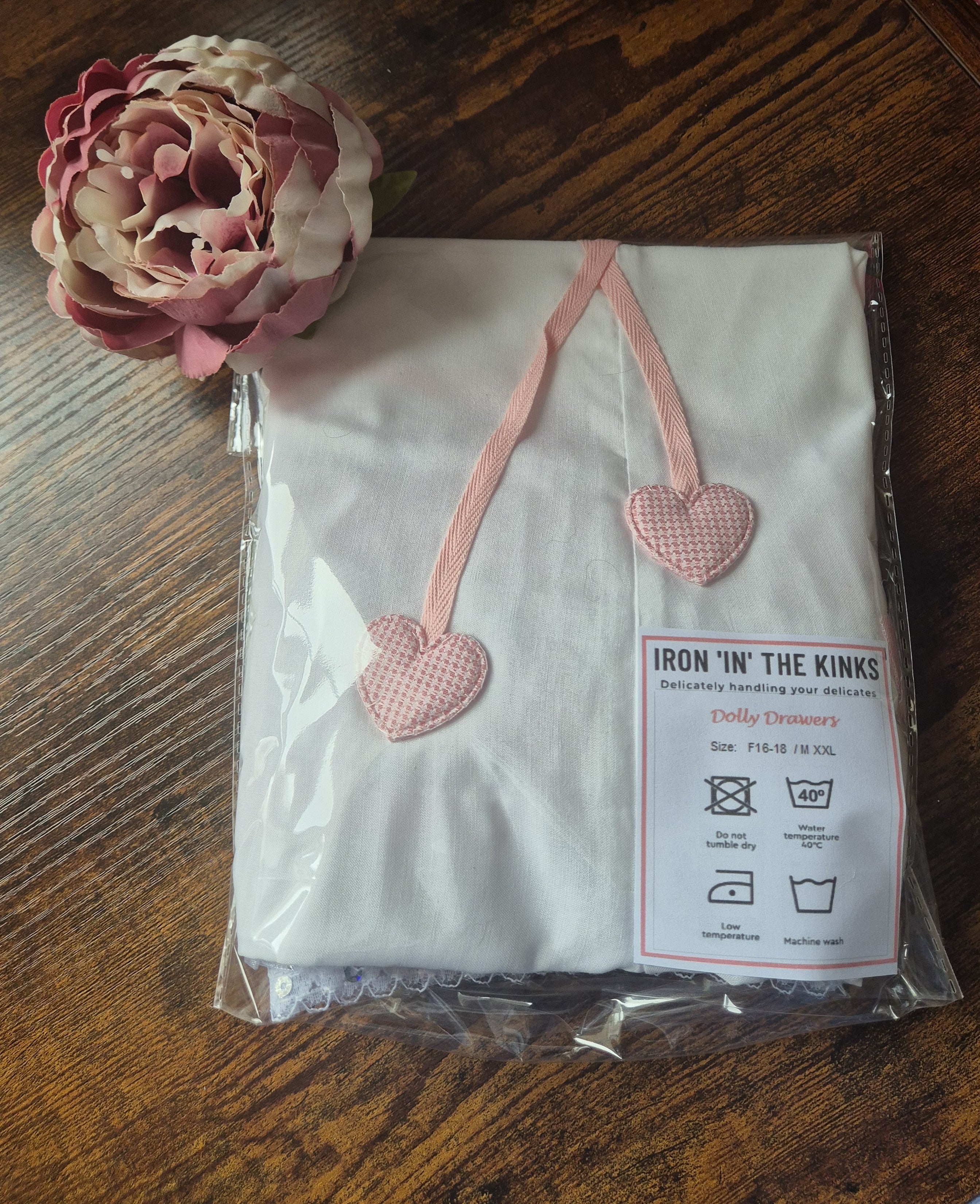 Packaged product with pink heart-shaped tags on a wooden surface with a flower.