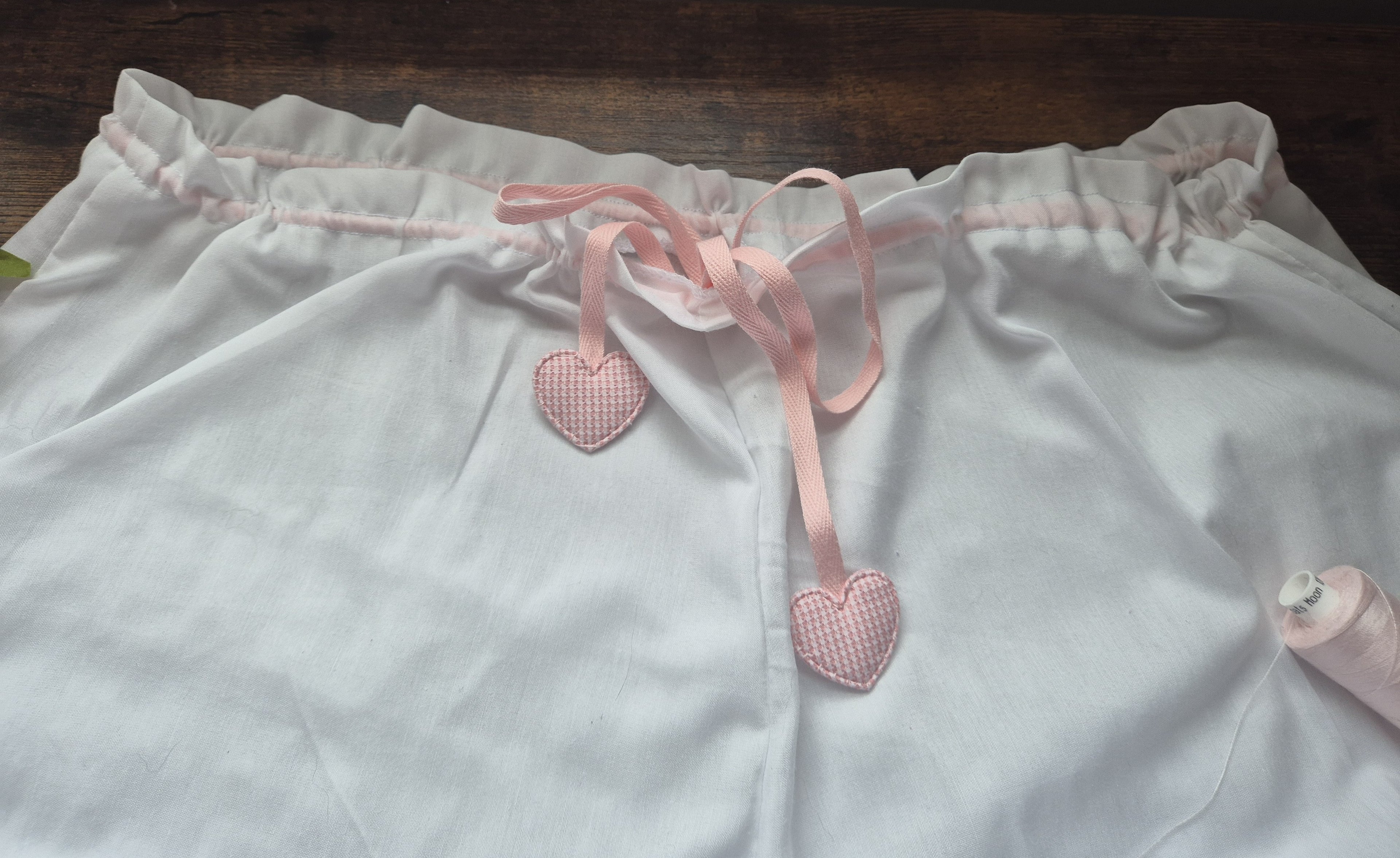 White drawstring cord waistband with pink heart-shaped tags on a wooden surface. sissy knickers, adult baby nappy cover, victorian style drawers, unisex