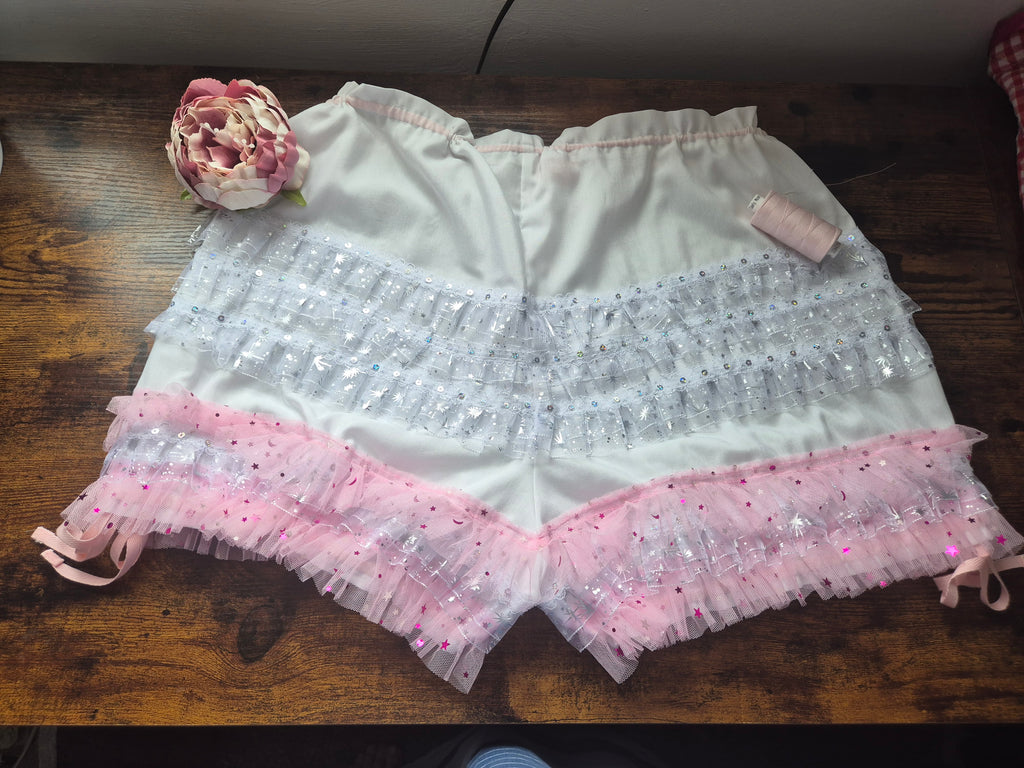 White shorts with pink trim on a wooden surface. sissy knickers, adult baby nappy cover, victorian style drawers, unisex