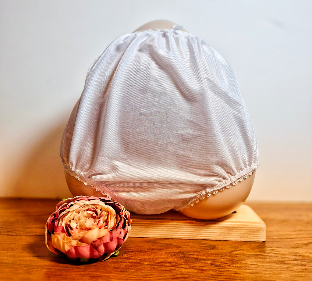 Front view - White lace-trimmed underwear on a wooden block with a decorative flower on a light background