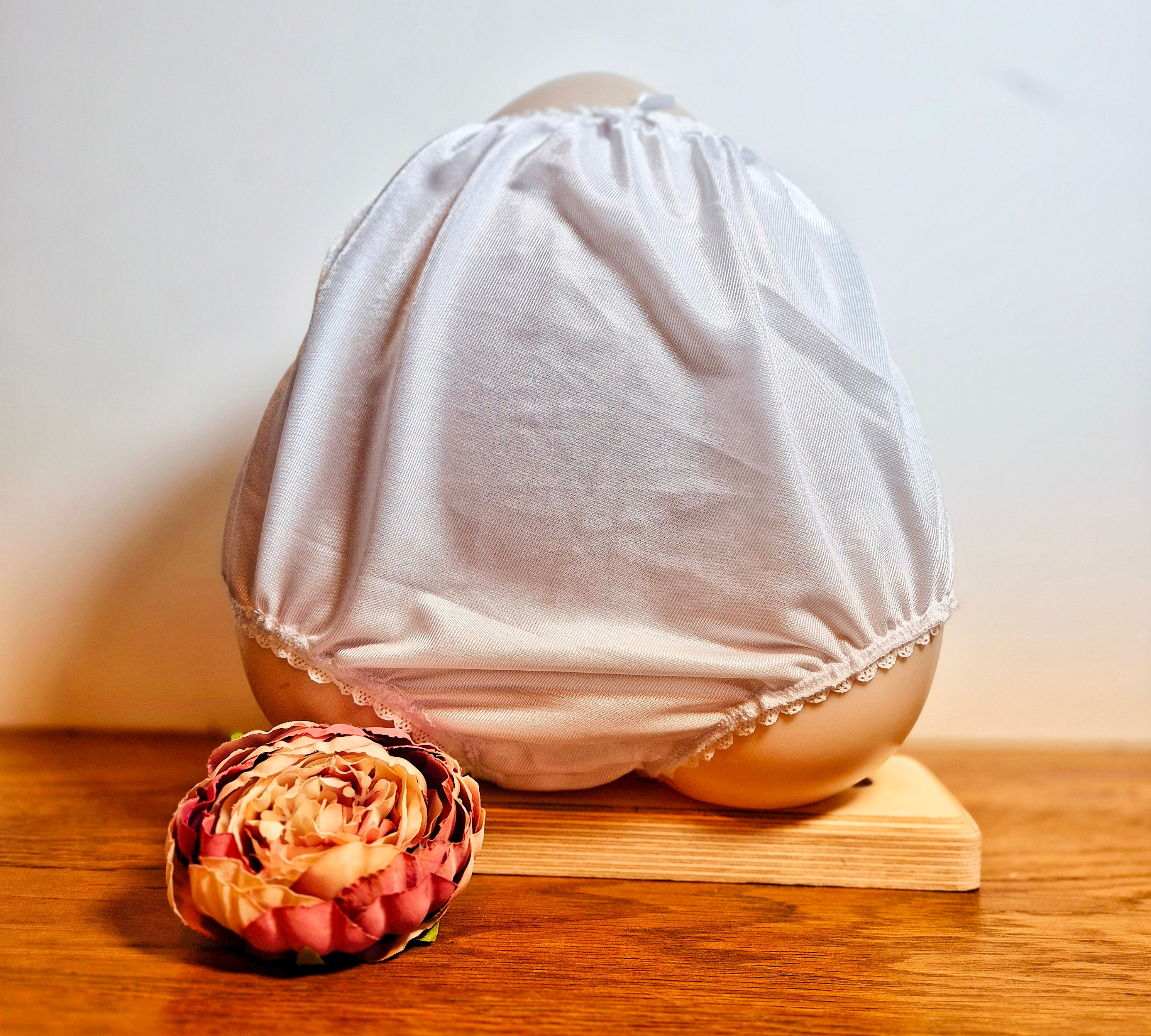 Front view - White lace-trimmed underwear on a wooden block with a decorative flower on a light background