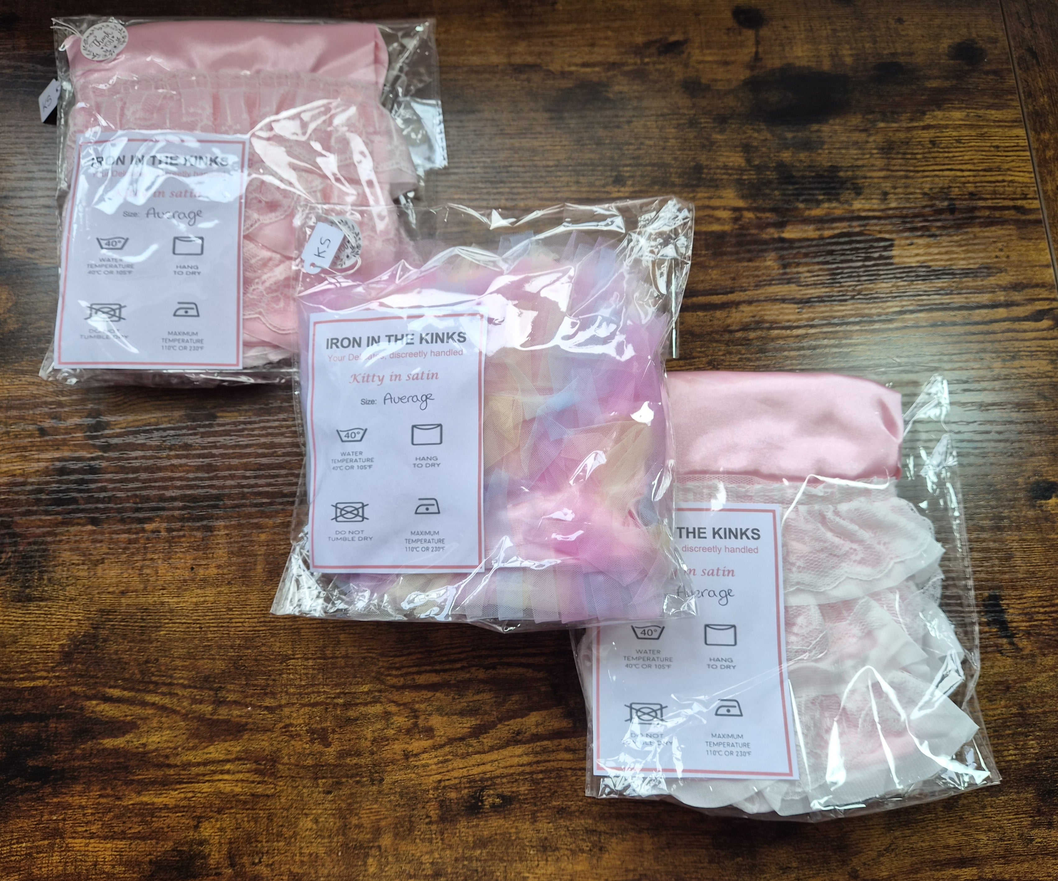 3 Packs of satin knickers showing ruffle lace details arranged on a wooden counter. 
