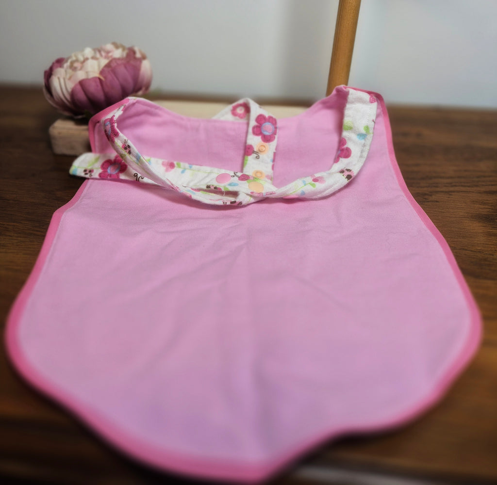 Pink adult baby bib (reverse side) with floral straps on a wooden surface