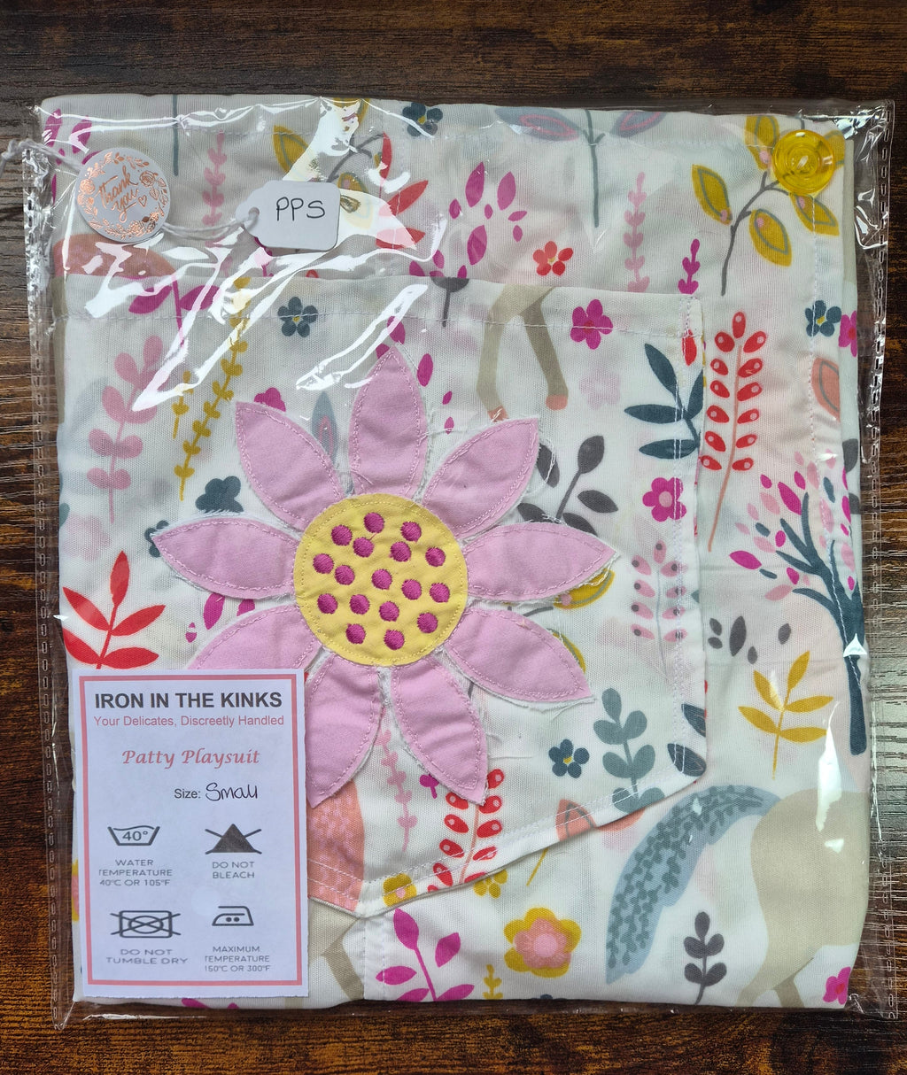 Iron in the Kinks Patty Playsuit in white  unicorn floral print with pink appliqué double daisy  motif in clear packaging with care label, size Small — wash at 40°C, do not bleach, do not tumble dry, iron max 150°C