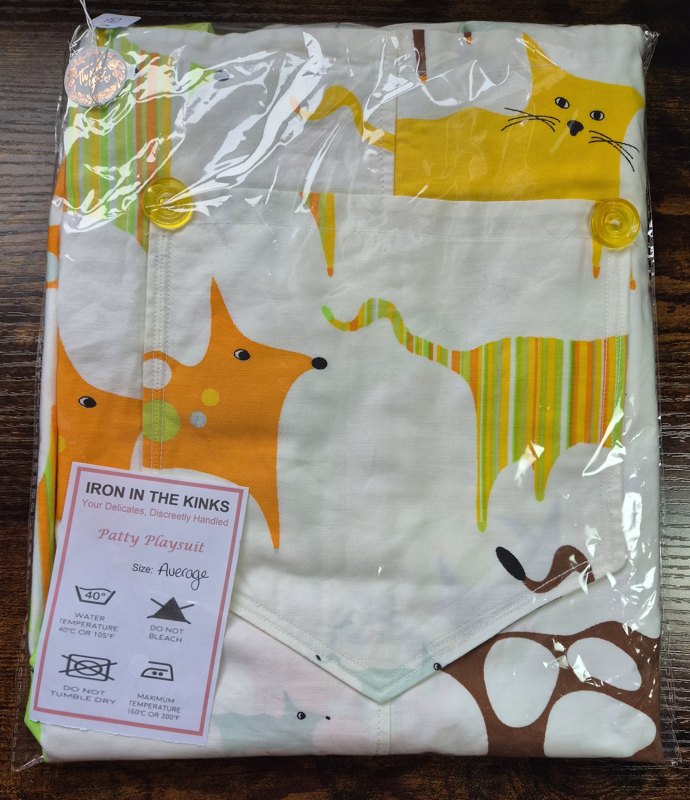 Iron in the Kinks Patty Playsuit, white with abstract animals in clear packaging. care label, size Average — wash at 40°C, do not bleach, do not tumble dry, iron max 150°C