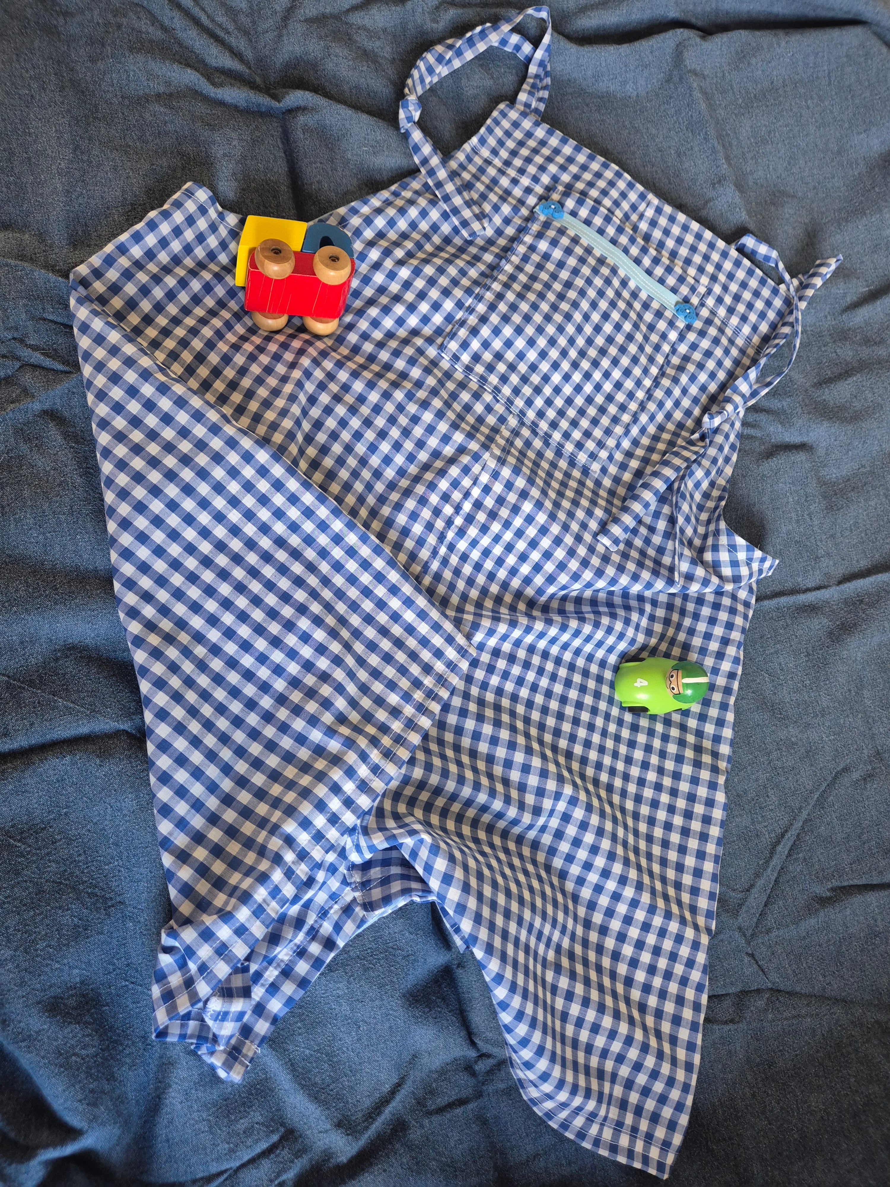 Blue gingham playsuit with car button details, lying on a blue fabric surface with toy cars. 