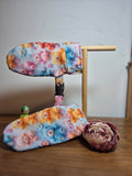 Smitten scratch cuffs with a stand showing safety clip, photographed on a dark wooden surface.