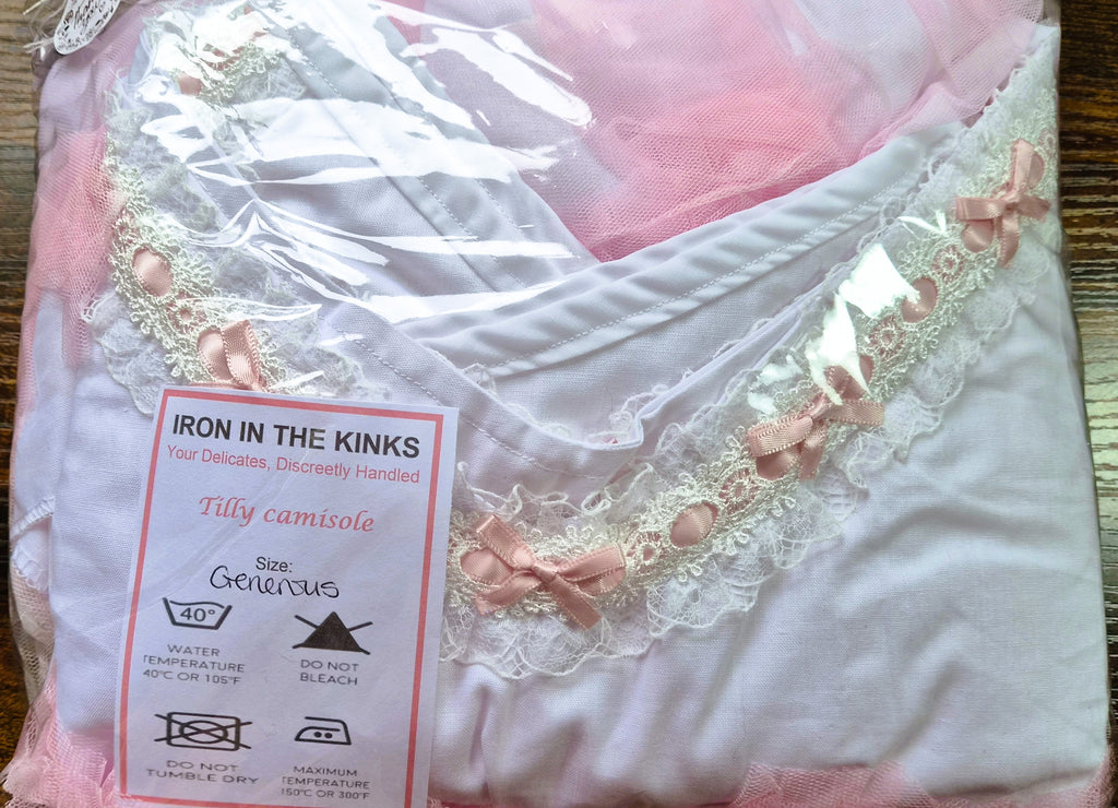 Iron in the Kinks Tilly Camisole in white with broderie anglaise and pink ribbon trim in clear packaging with care label, size Generous — wash at 40°C, do not bleach, do not tumble dry, iron at max 150°C