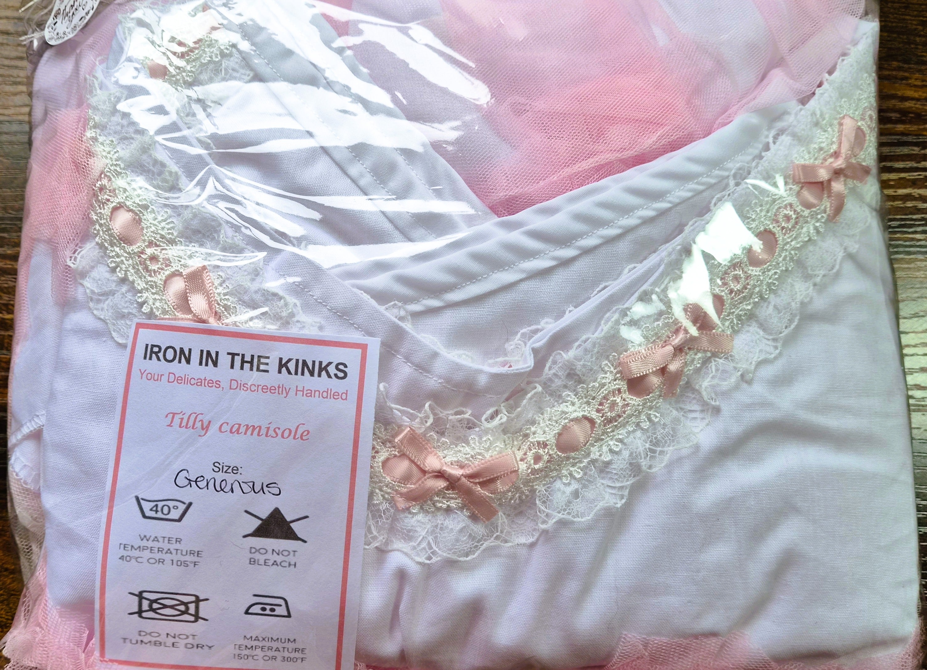 Iron in the Kinks Tilly Camisole in white with broderie anglaise and pink ribbon trim in clear packaging with care label, size Generous — wash at 40°C, do not bleach, do not tumble dry, iron at max 150°C