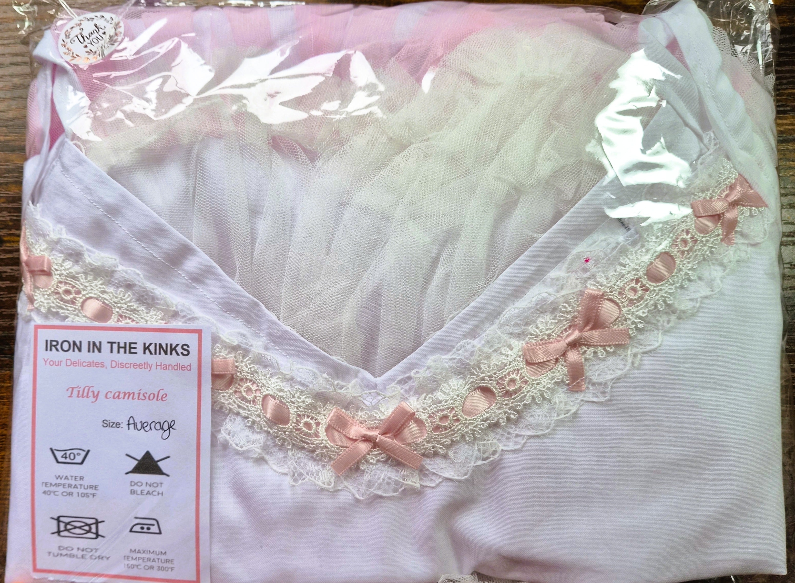 Iron in the Kinks Tilly Camisole in white with broderie anglaise and pink ribbon trim in clear packaging with care label, size Average — wash at 40°C, do not bleach, do not tumble dry, iron at max 150°C